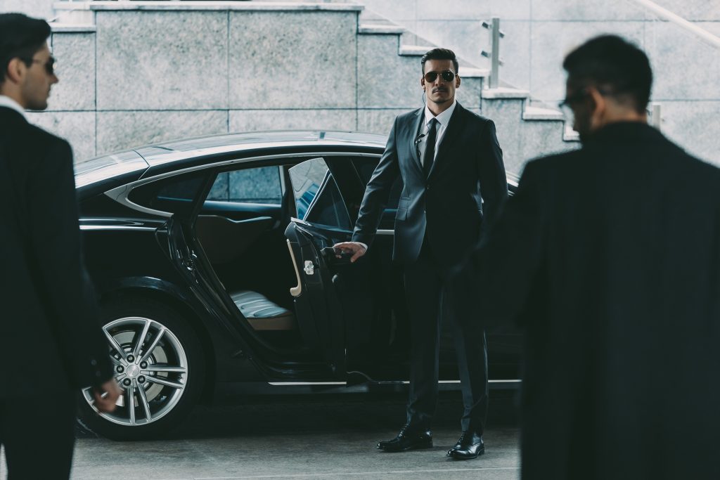 bodyguard in sunglasses opening car door to businessman